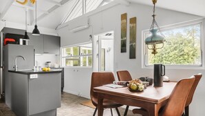 A modern kitchen with a central island, a dining table with chairs, and a large window providing a view of greenery. - 2 bedroom nice home in Karrebæksminde (Karrebæksminde)