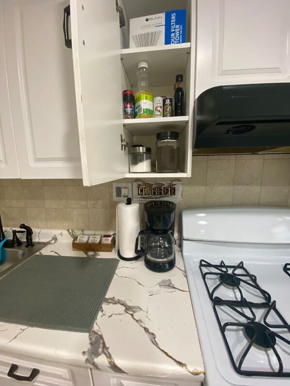 A kitchen with a white stove, a coffee maker, and a cabinet with various items.