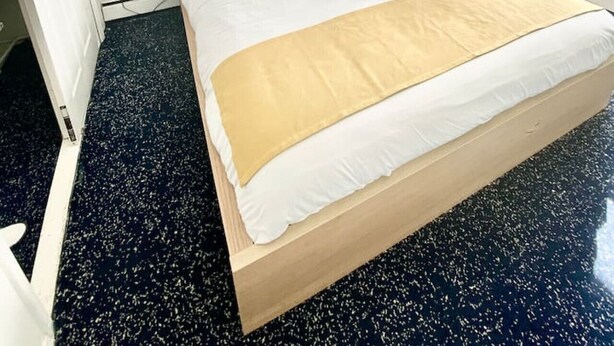 Habitación de hotel con una cama grande, un cuadro de un paisaje urbano en la pared, una mesita de noche con lámpara y una ventana con cortinas.
