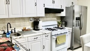 Una cocina con armarios blancos, un refrigerador de acero inoxidable, una estufa a gas y una cafetera.