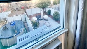 Una ventana con vista a un patio trasero, que incluye mobiliario exterior y un hogar para fuego.