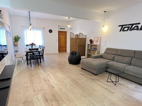 A modern living room with a grey sofa, a dining area with a table and chairs, and a large black bean bag. - Complete rural house for 6 people in Pedralba (Valencia). (Pedralba)