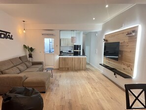A modern living room with a sofa, a TV mounted on a wooden wall, and a kitchen in the background. - Complete rural house for 6 people in Pedralba (Valencia). (Pedralba)