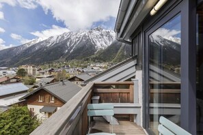 Un balcón con vista a una cadena montañosa, bancos de madera y un edificio moderno con amplias ventanas.