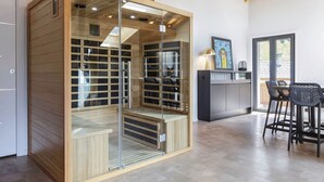 Una cocina moderna con sauna de vidrio, vigas de madera y un comedor con sillas negras.