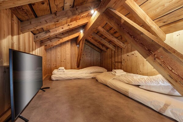 Un dormitorio en ático con techos altos, vigas de madera a la vista, dos camas y un televisor de pantalla plana.