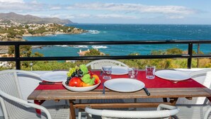 A dining table with plates, cutlery, and a fruit bowl set against a scenic ocean view.
