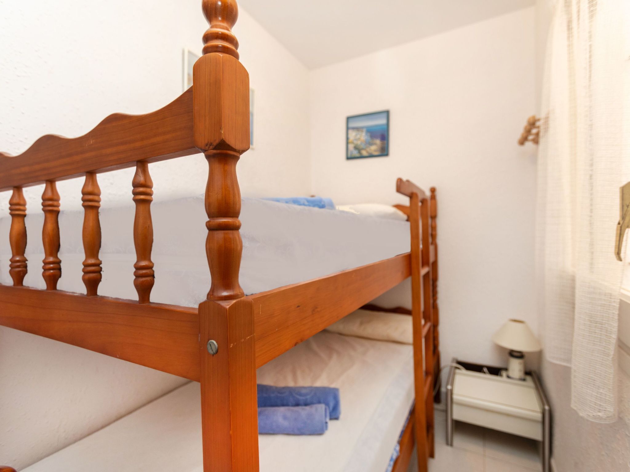 Un lit superposé en bois dans une pièce aux murs blancs, avec une petite table de chevet et une lampe.