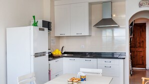 Een kleine keuken met witte kastjes, een zwart aanrecht en een RVS afzuigkap. Er staat een tafeltje met een schaal vol citroenen en een mandje muffins.
