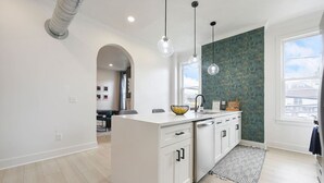 A modern kitchen with white cabinetry, a central island, pendant lighting, and a view of the city through a large window. - ★ HostWise Stays ★ Skyline City Views & Rooftop Bar at Mt. Washington (Pittsburgh)