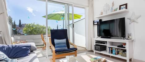 A modern living room with a sofa, a chair, a coffee table, and a TV stand with a flat-screen TV and a bookshelf.