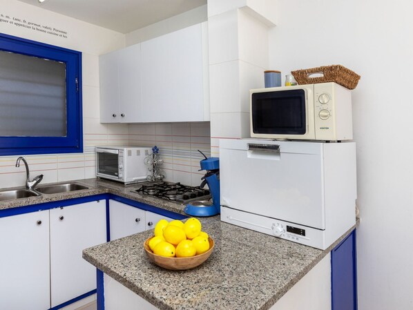 Una cocina con armarios blancos, un ventanal con marco azul, un microondas, un tostador, una estufa y un bol de limones en la encimera.