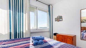 A bedroom with a bed, a wooden dresser, a window with curtains, and a wall with a clock and pictures. - Apartment Grifeu by Interhome (Llançà)