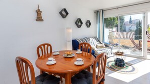 A dining area with a round wooden table, four chairs, and a blue sofa in the background. - Apartment Grifeu by Interhome (Llançà)