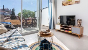 A modern living room with a sofa, a TV, and a dining area visible through a sliding glass door. - Apartment Grifeu by Interhome (Llançà)