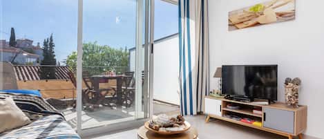 A modern living room with a sofa, a TV, and a dining area visible through a sliding glass door.