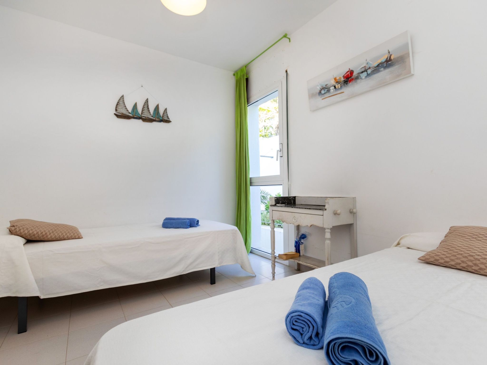 A room with two beds, a small desk, and a window with a green curtain.