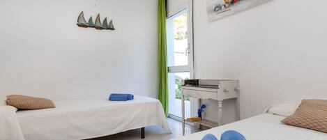 A room with two beds, a small desk, and a window with a green curtain.