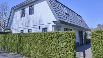 Una moderna casa a due piani con tetto spiovente, un portico coperto e un siepe ben curata davanti.