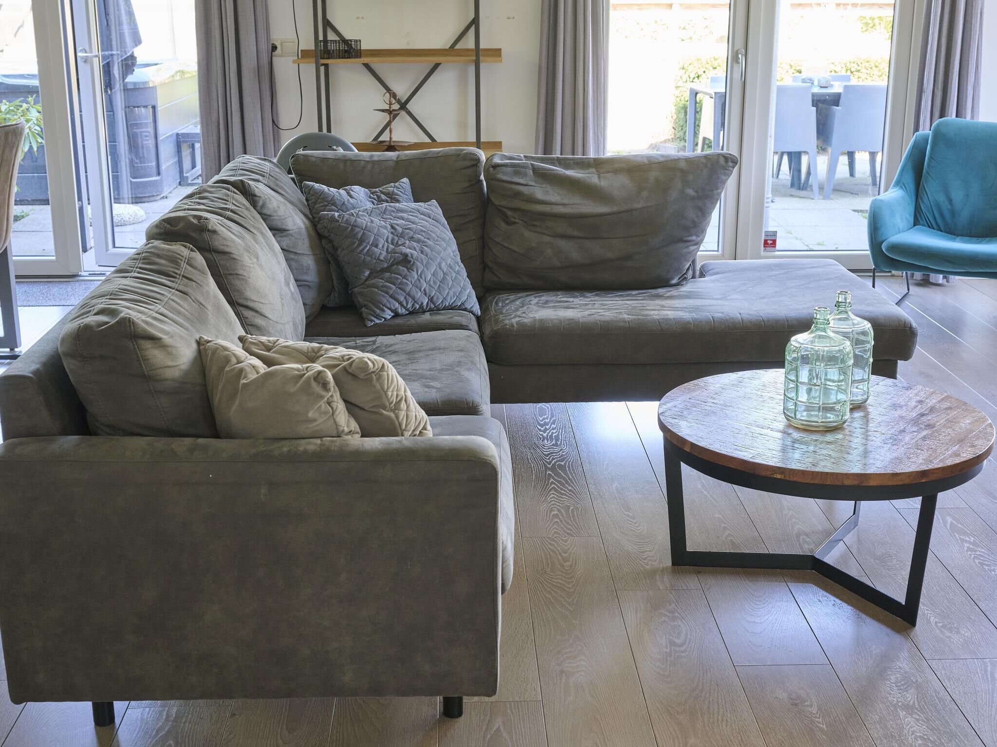 Een moderne woonkamer met een hoekbank, een ronde salontafel en uitzicht op de omgeving door een glazen deur.