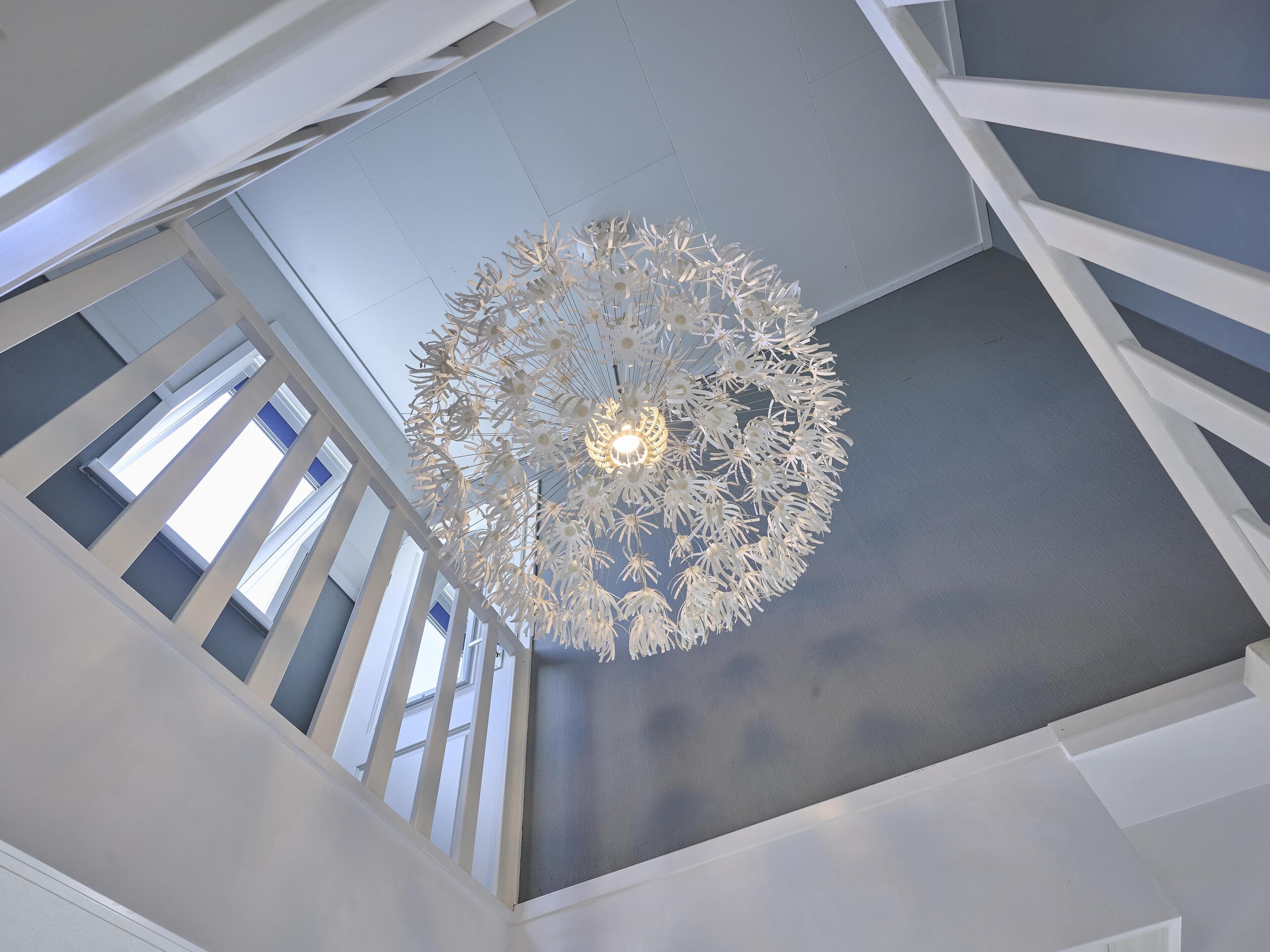Een modern interieur met een bijzondere plafondlamp en witte leuning.