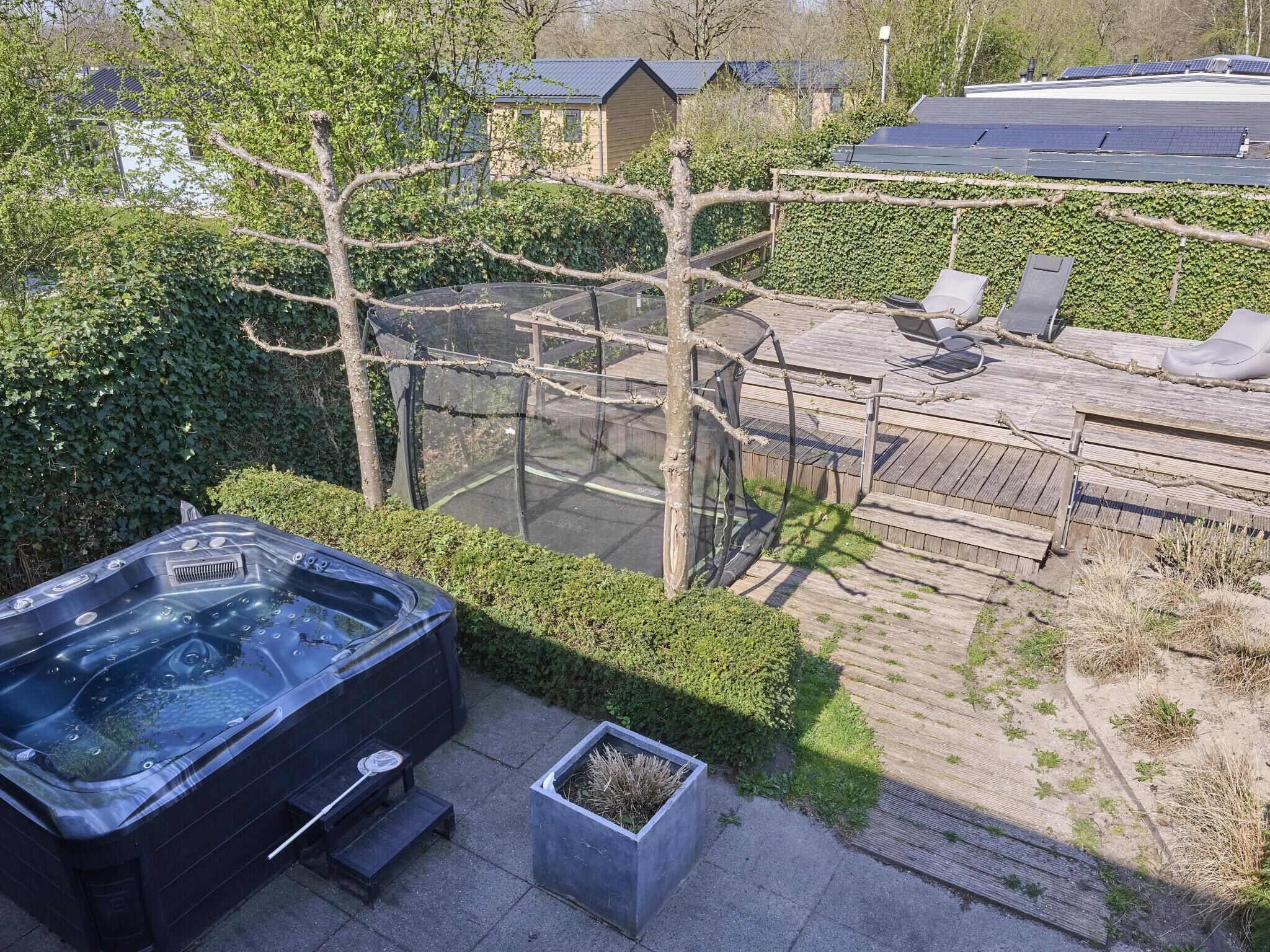 Una vasca idromassaggio in un giardino con un patio in legno e un recinto in vetro.