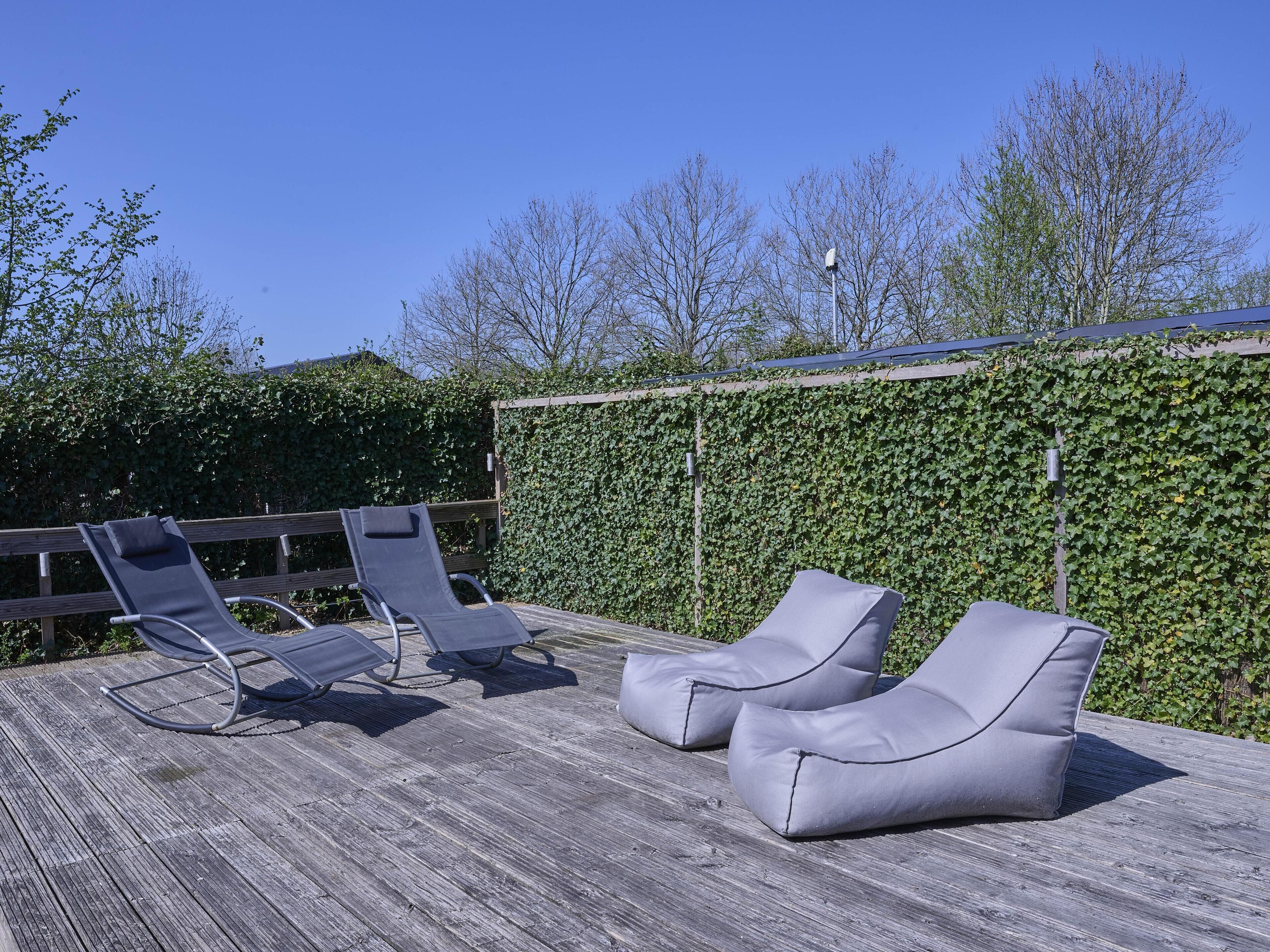 Eine Holzterrasse mit zwei Liegestühlen und einer mit Efeu bewachsenen Mauer.