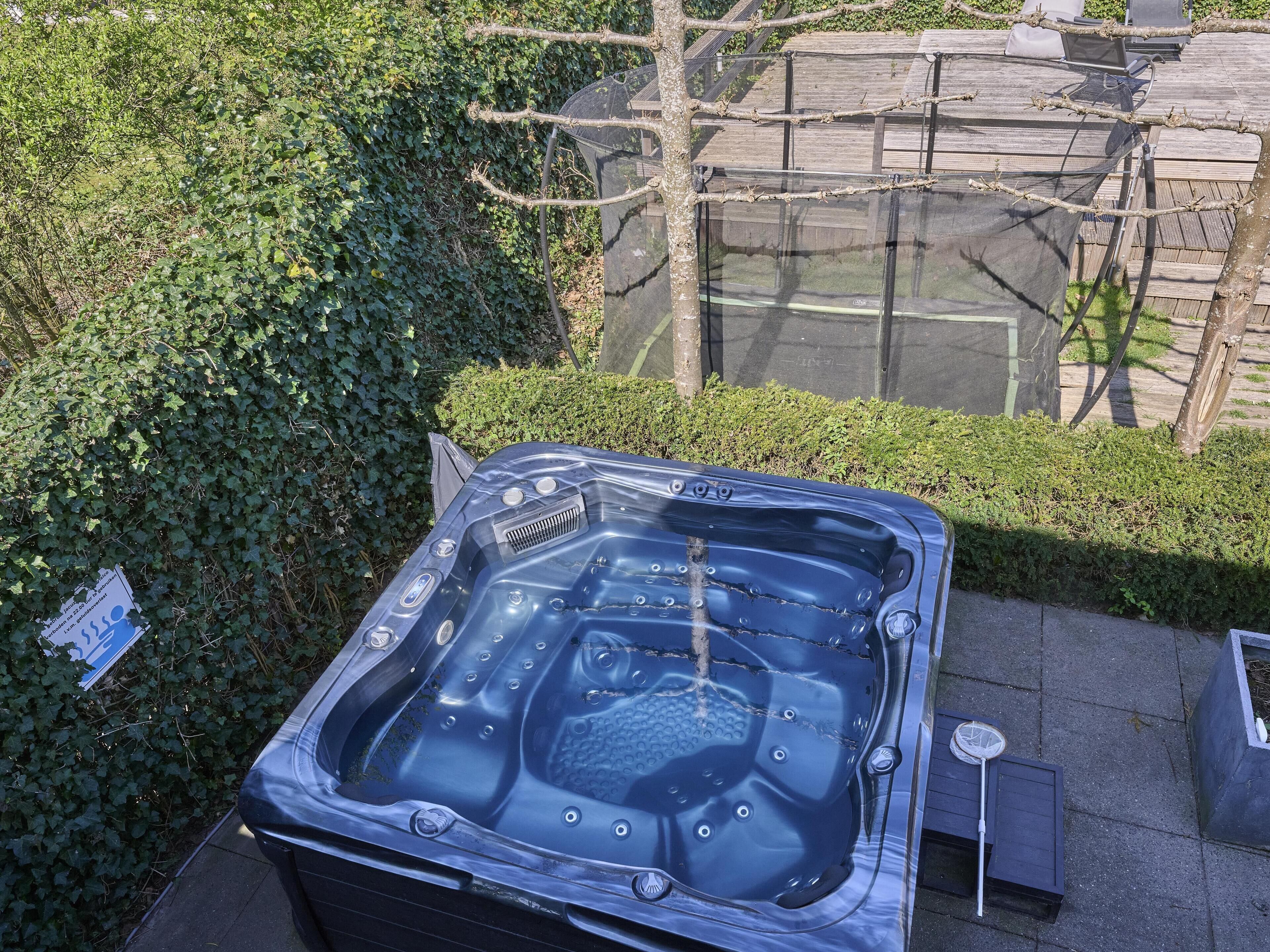 Een hottub buiten, met een houten terras en een haag op de achtergrond.