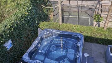 Een hottub buiten, met een houten terras en een haag op de achtergrond.