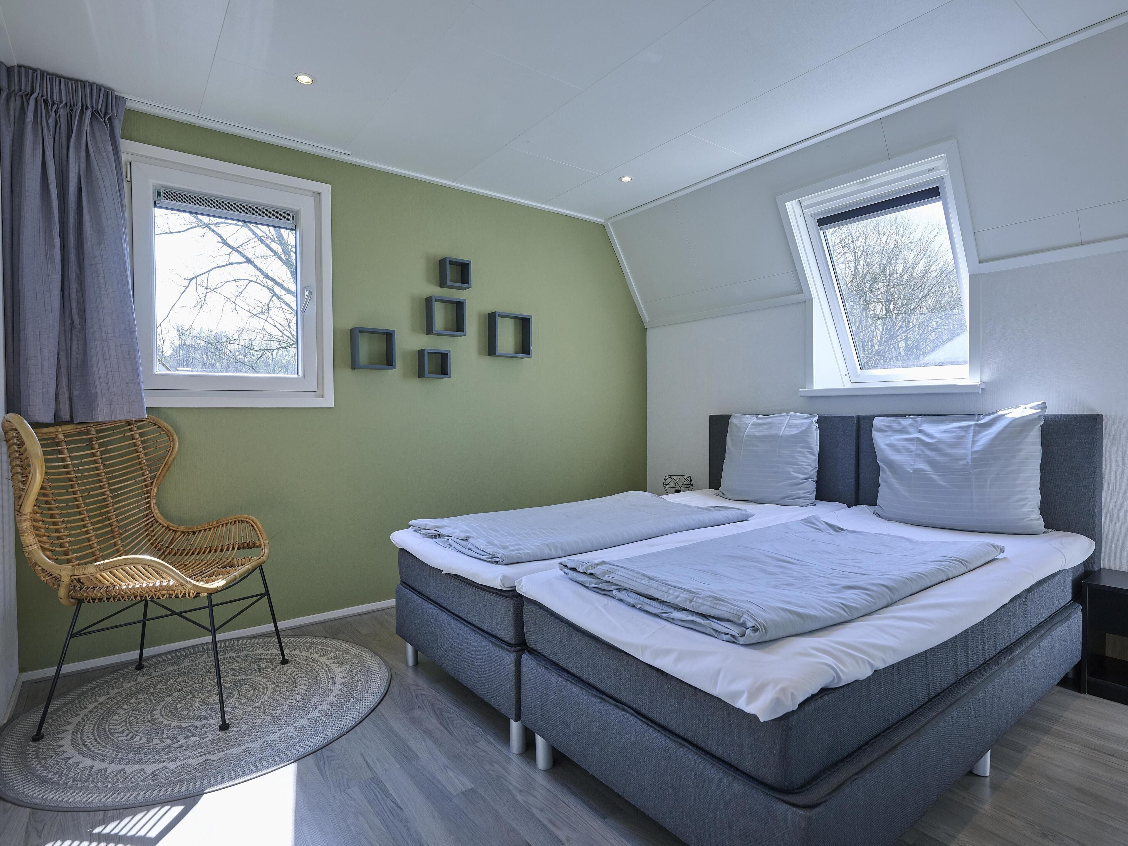 A bedroom with a bed, two windows, a chair, and wall decorations.