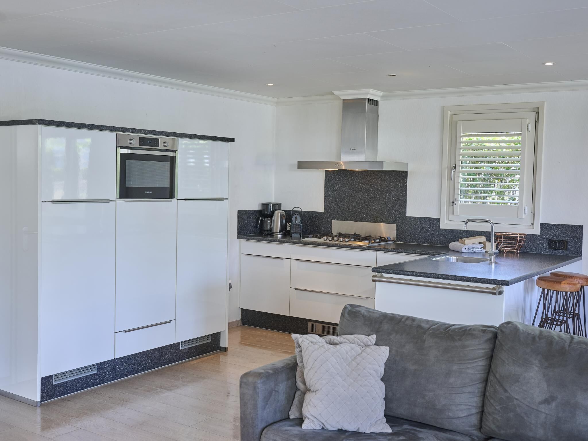 A modern kitchen with white cabinetry, a built-in oven, a gas stove, and a window with blinds.