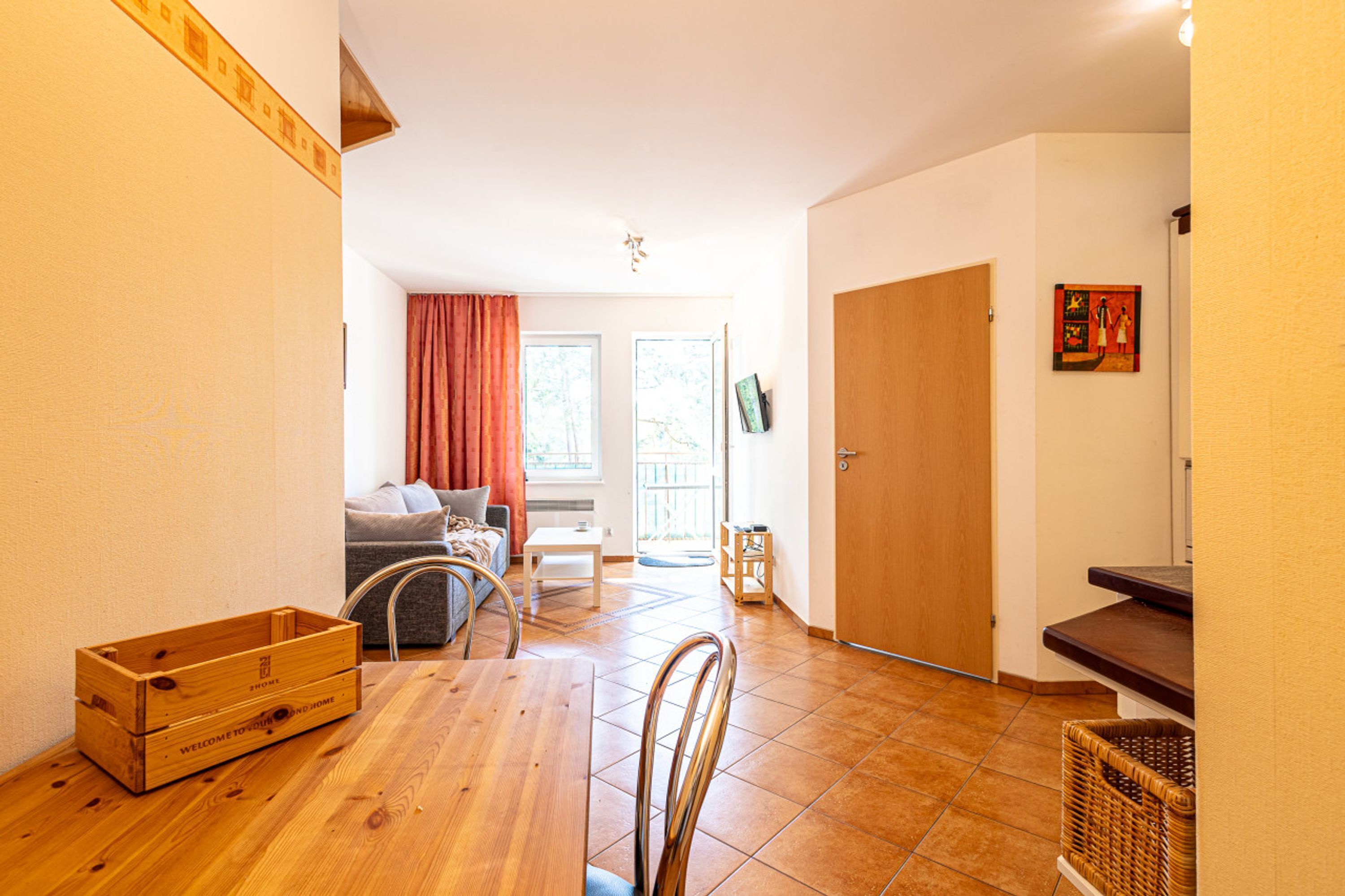 Una habitació àmplia amb terra de fusta, una taula de dinar amb cadires, un sofà, una taula petita i una porta que dona a una altra habitació.