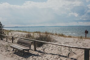 A wooden bench on a sandy beach with a wooden fence and a signpost in the background. - Lento Dla Rodzin i Grup Blisko Promenady (Miedzyzdroje)