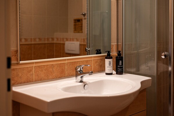 Une salle de bain avec un lavabo blanc, un miroir et deux flacons de produits de toilette de la marque 2HOME.