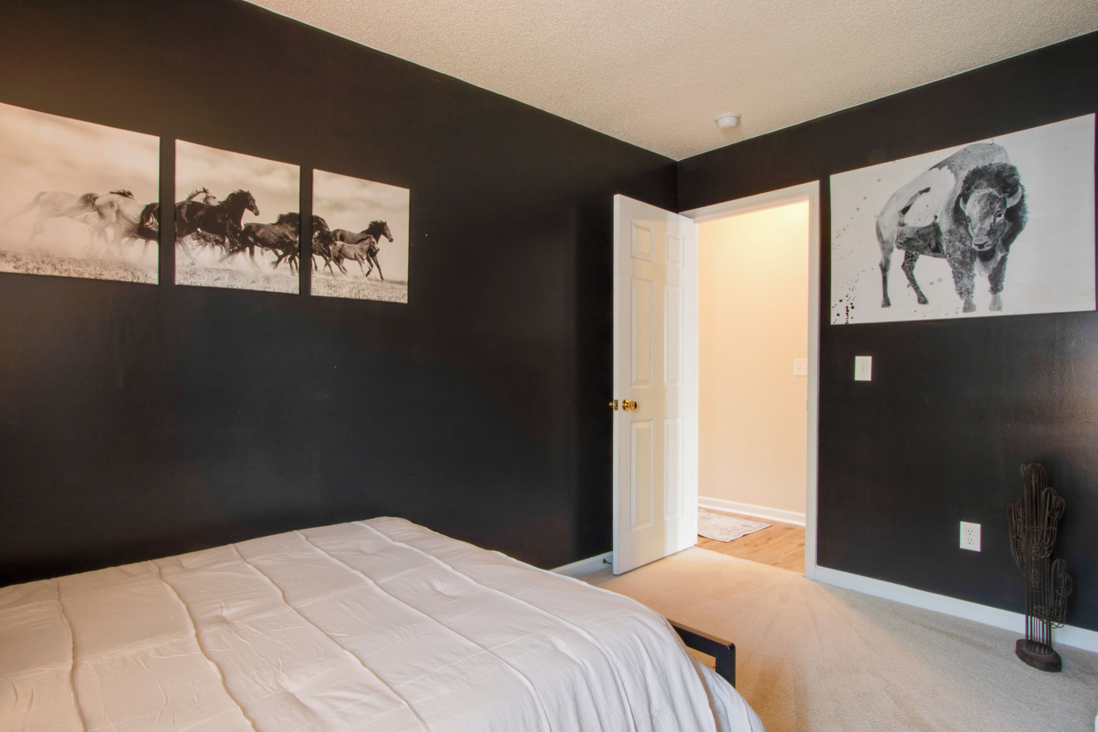 Un dormitorio con una cama grande, una puerta que da a otra habitación y tres obras de arte colgadas en la pared que representan caballos y un toro.