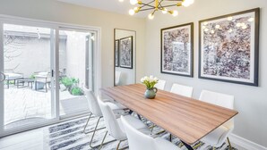 Un comedor con una mesa de madera, sillas blancas, un jarrón con flores y arte abstracto en las paredes.