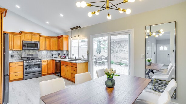 Una cocina moderna con armarios de madera, electrodomésticos de acero inoxidable y una zona de comedor con mesa de madera y sillas blancas.