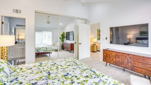 Un dormitorio moderno con cama, televisor, armario y puerta corredera que da a otra habitación.
