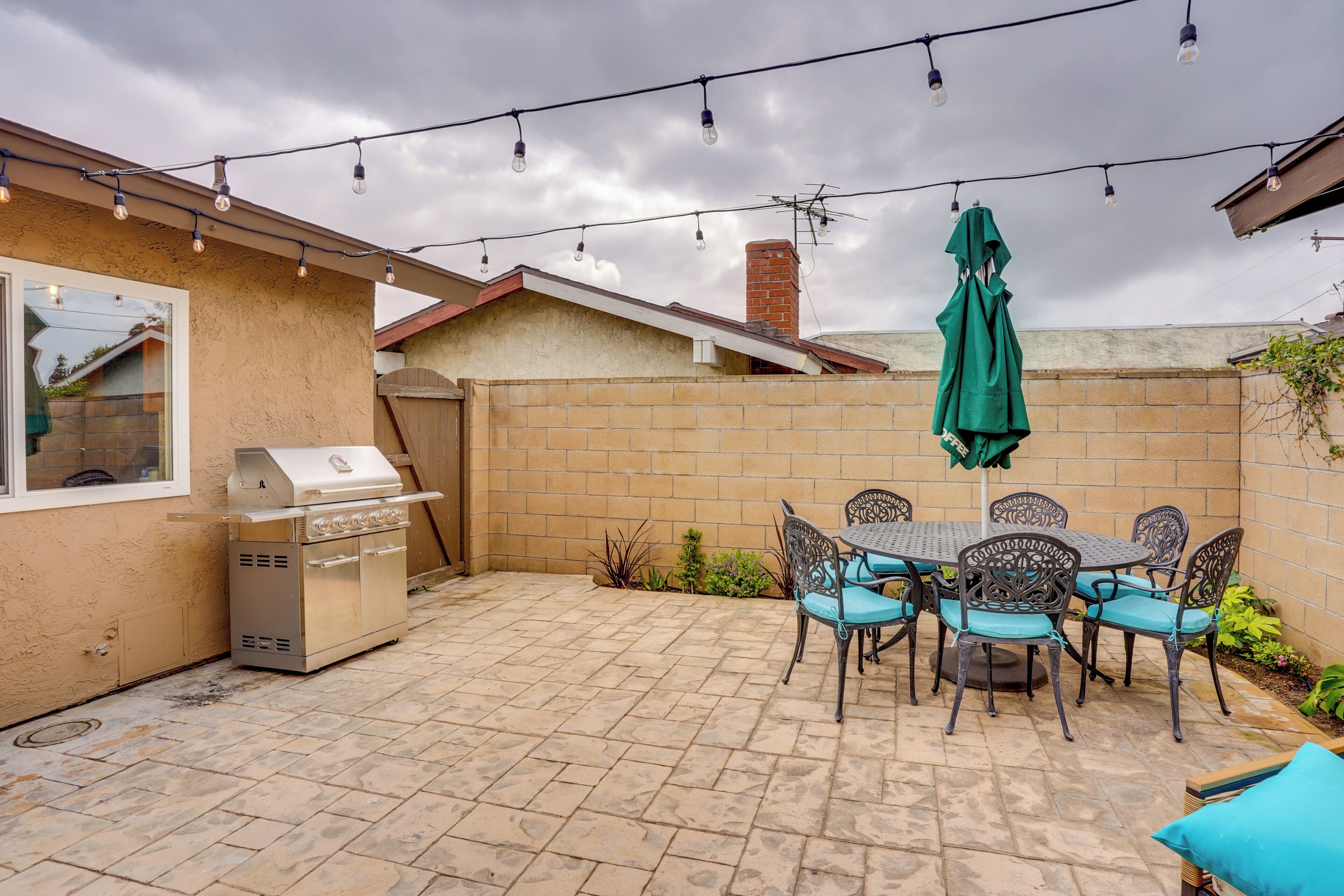 A backyard with a barbecue grill, a table with chairs, and string lights.