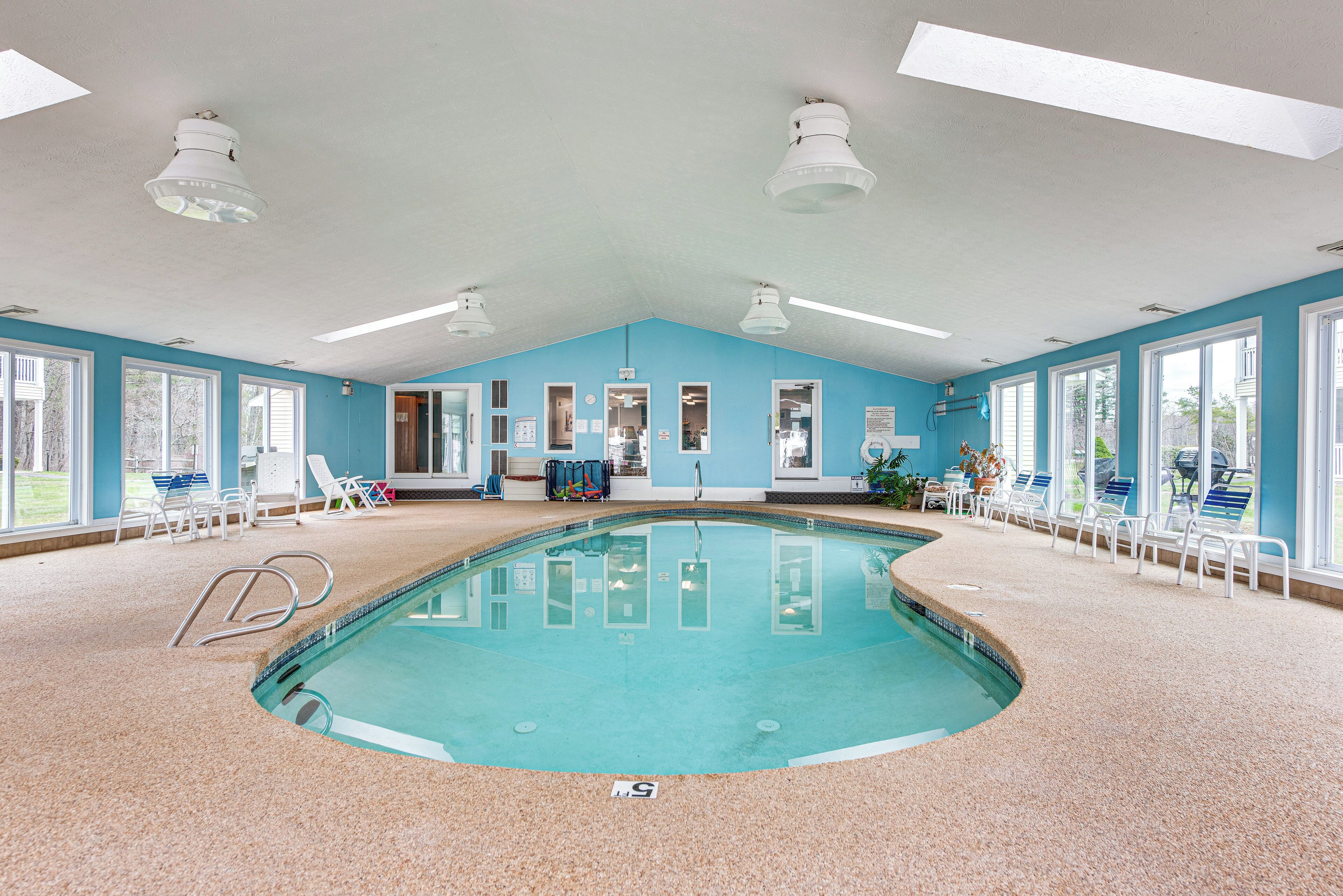 An indoor swimming pool with clear blue walls, multiple windows, and ceiling lights.
