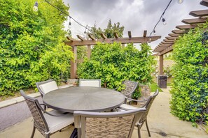 Eine Terrasse im Freien mit rundem Tisch und Stühlen, umgeben von üppigem Grün und einer Pergola.