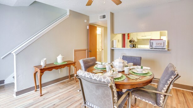 Un coin repas avec une table ronde, des chaises et un ventilateur de plafond. Un escalier est visible sur la gauche.