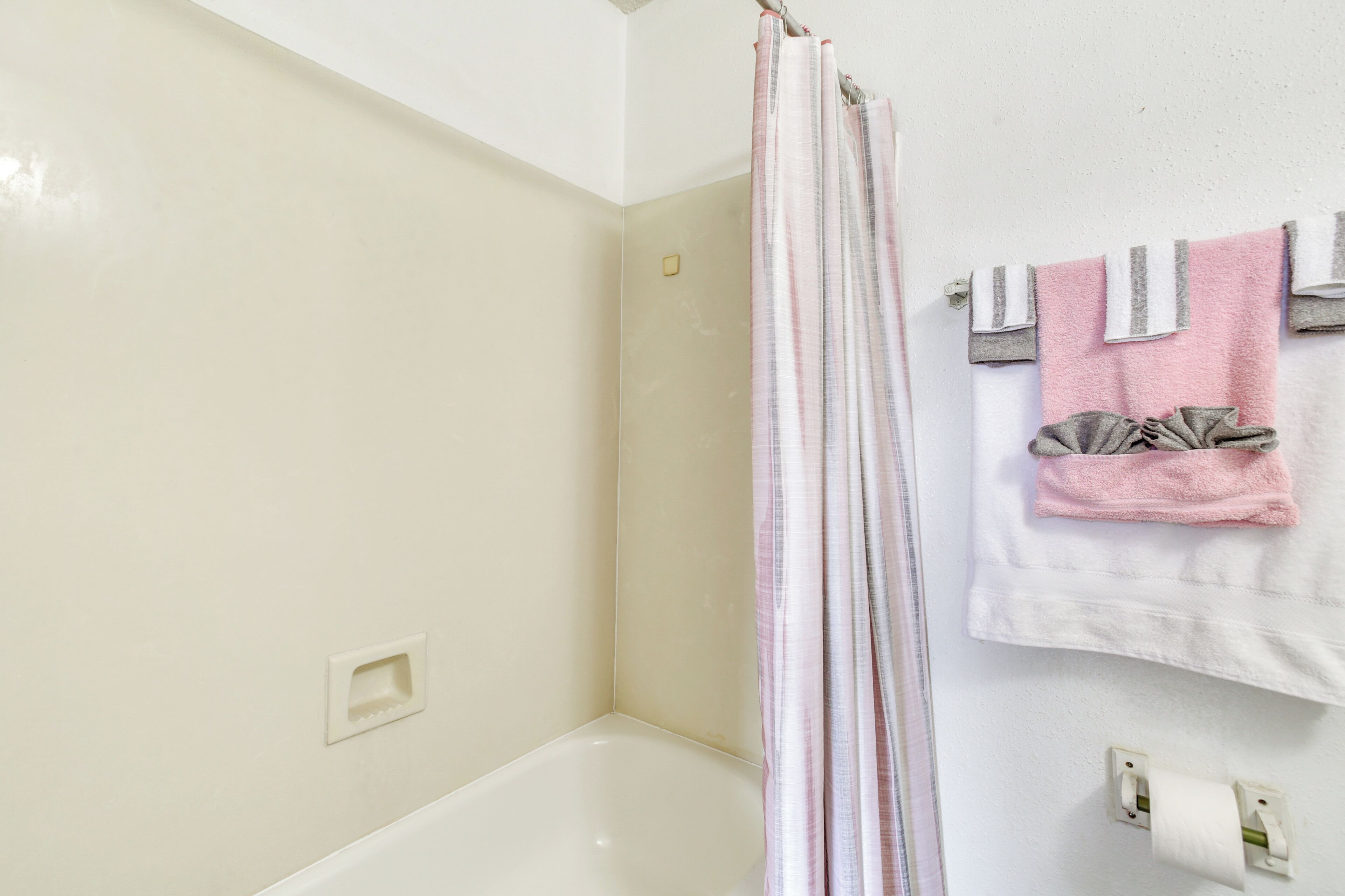 Ein Badezimmer mit einer weißen Badewanne, einer Duschvorhang und einem Handtuchhalter mit mehreren Handtüchern.