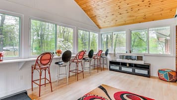 Un espace repas moderne avec un plancher en bois, un tapis à motifs noirs et rouges, et un mur blanc agrémenté d’une étagère intégrée pour la télévision.