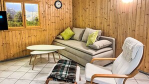 Ett mysigt rum med träväggar, en soffa, en fåtölj, ett litet bord och en tv på väggen.