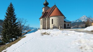 En kyrka byggd av sten med ett rött tak och ett klocktorn, omgiven av snö och berg.