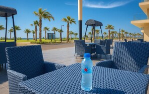Relax in a casual outdoor dining area with comfortable wicker chairs and tables, surrounded by palm trees.