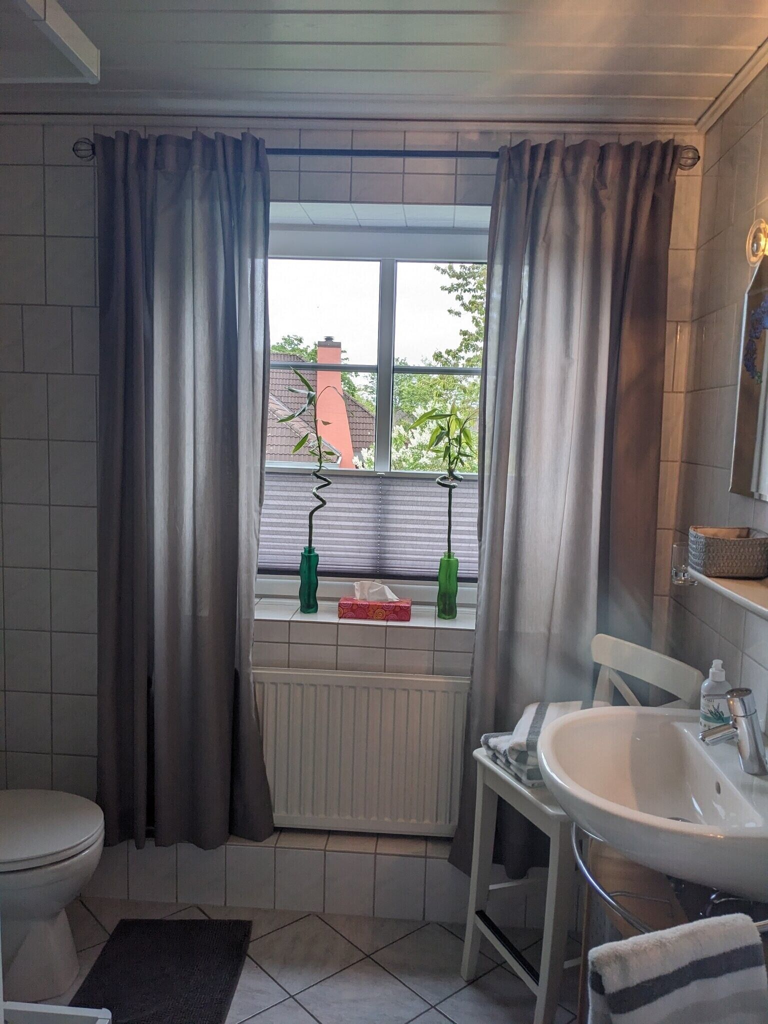 Et badeværelse med toilet, håndvask og et vindue med gardiner.