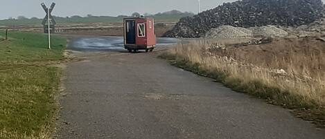 Een landelijke weg met een rode mobiele toiletten en een spoorwegovergang.