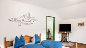 Ein Schlafzimmer mit einem Bett, Kissen, einem Wandbild, einem Fernseher und einem kleinen Tisch.